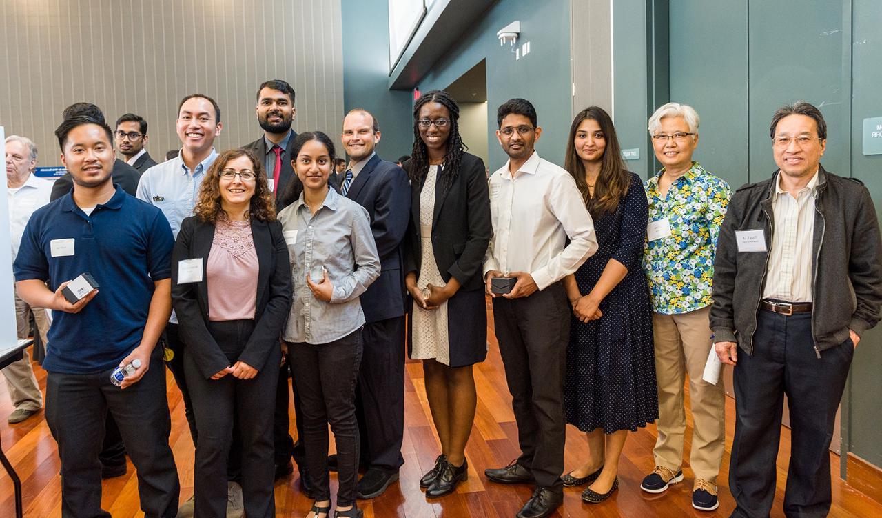 A formally dressed group of students and faculty stand together and smiling.